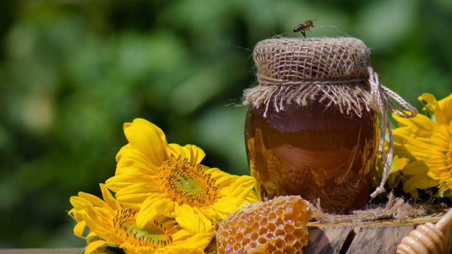A jar of organic, natural honey with a honeycomb piece and sunflowers, emphasizing freshness and quality.