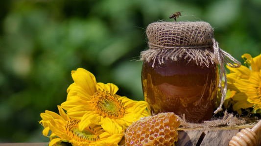 A jar of organic, natural honey with a honeycomb piece and sunflowers, emphasizing freshness and quality.